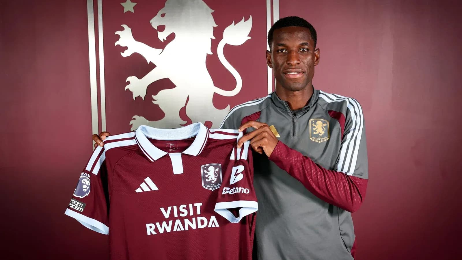 Игрок держит футболку Aston Villa на фоне логотипа