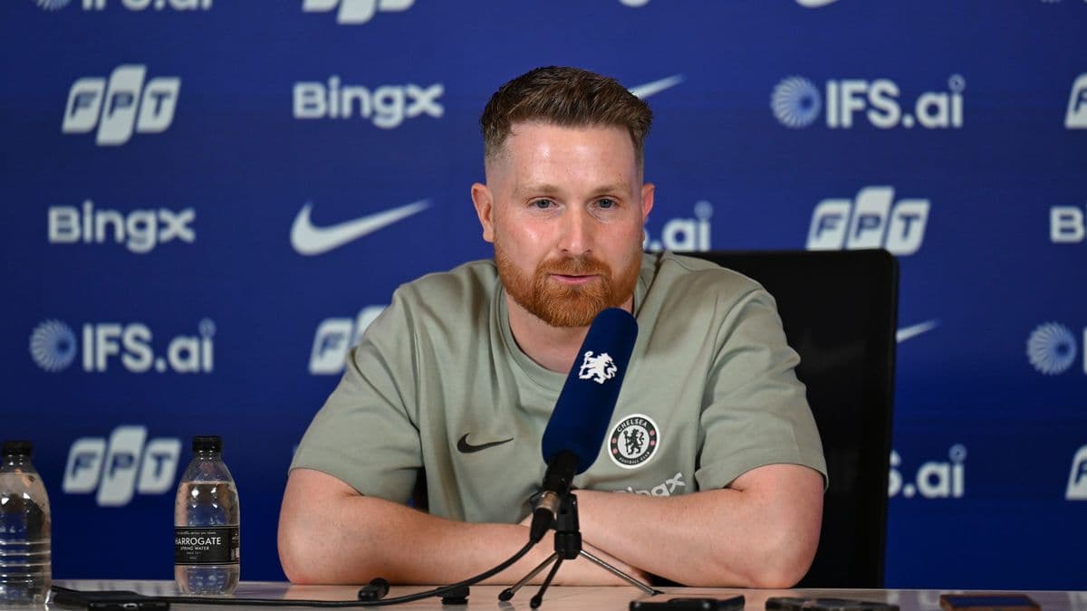 Человек на пресс-конференции с логотипом Chelsea